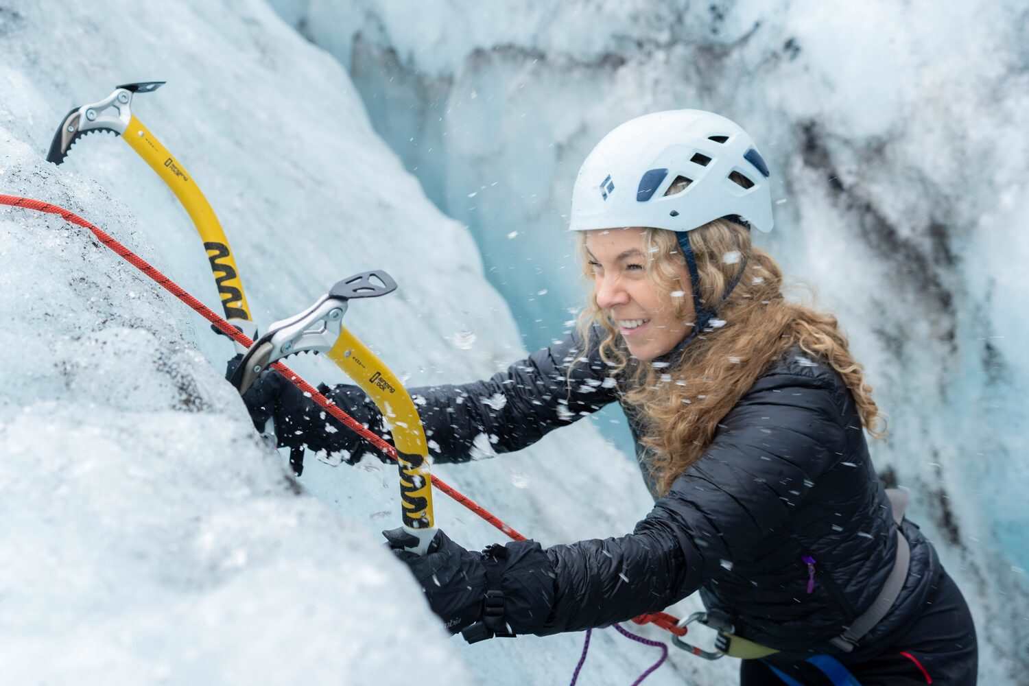 Female in white helmet close up climbing glacier with yellow ice axes