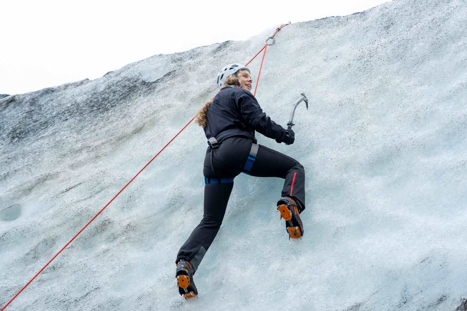Female using ice axes to climb glacier ice wall at Sólheimajökull 